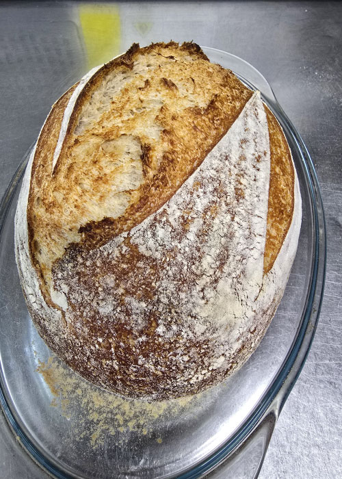 An oval loaf of sourdough bread on a silver plate dusted with flour.