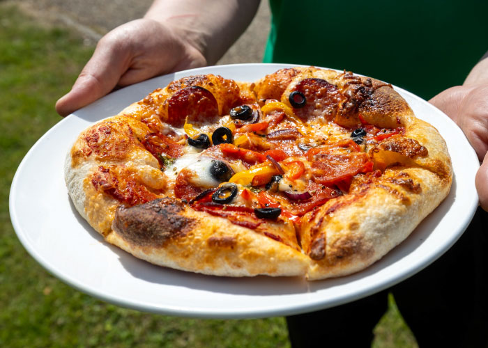 Hands holding a plate with a pepperoni sourdough pizza from The Ash Pub in Stansted.