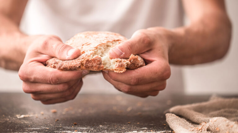Two hands tearing open a loaf of fresh sourdough bread.